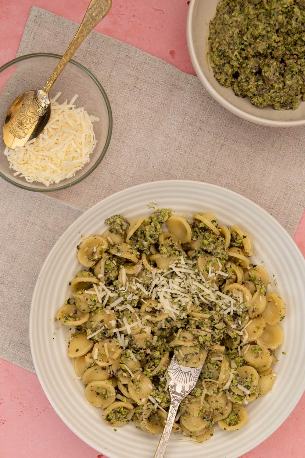 White bowl filled with gluten free pasta fagioli topped with grated parmesan and chopped parsley with a spoon on the side, a bowl of soup in the background and a striped napkin on the side. 
