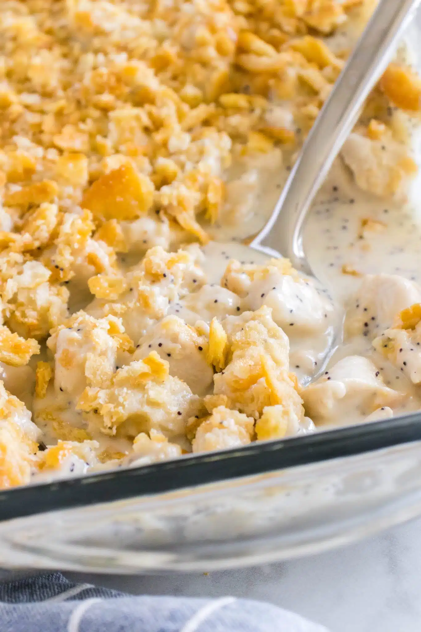 Large serving spoon resting in a glass baking dish filled with poppy seed chicken casserole. 
