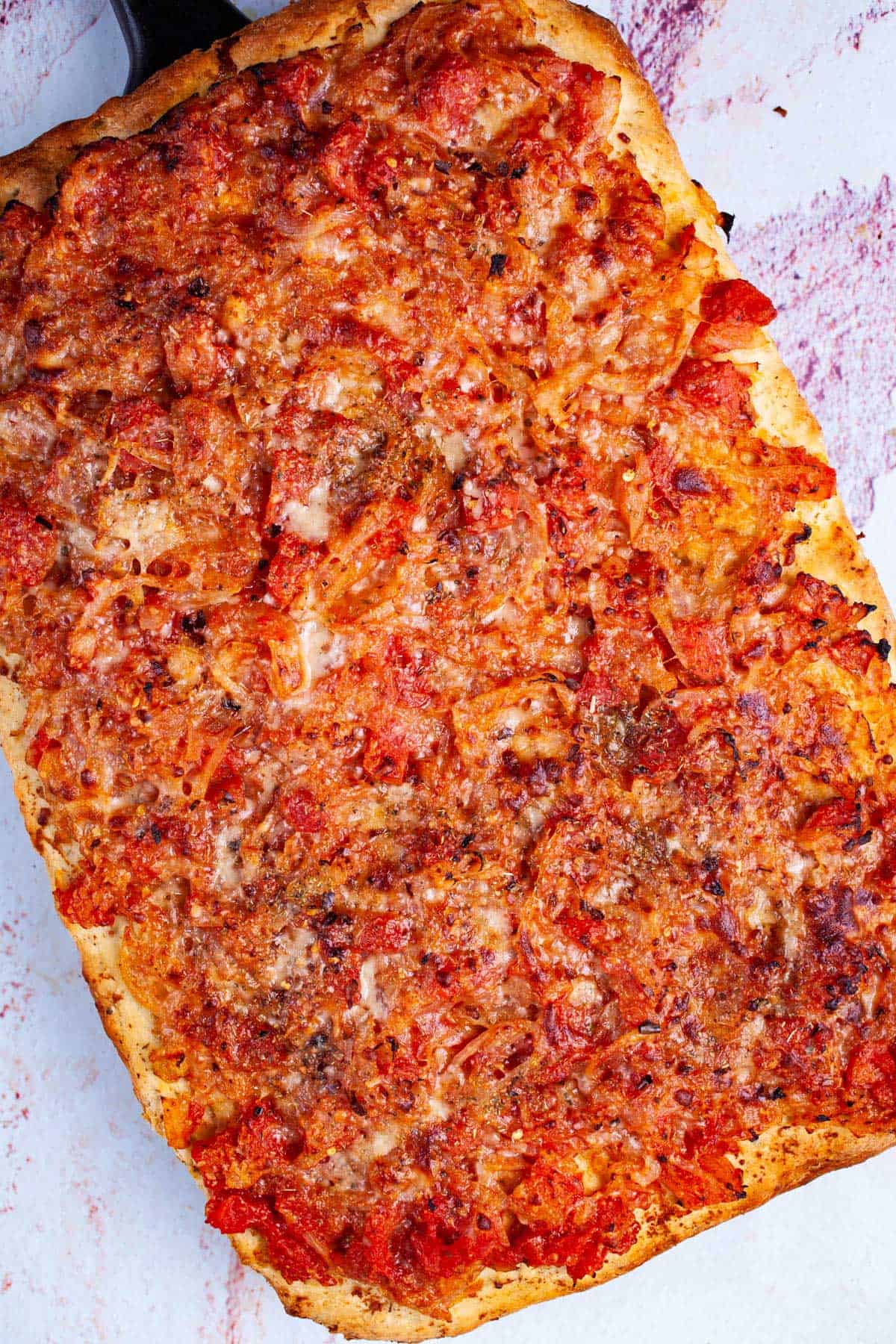 Thick-crust Sicilian pizza with onion-based toppings on a cutting board.
