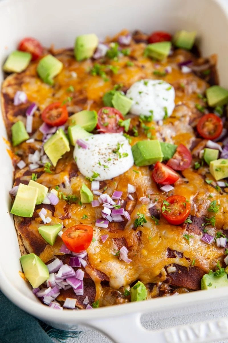 Big white casserole dish of beef enchiladas with corn tortillas. 
