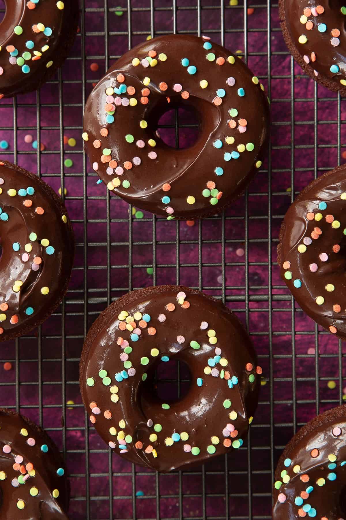 Unique chocolate donuts with sprinkles on a cooling rack.