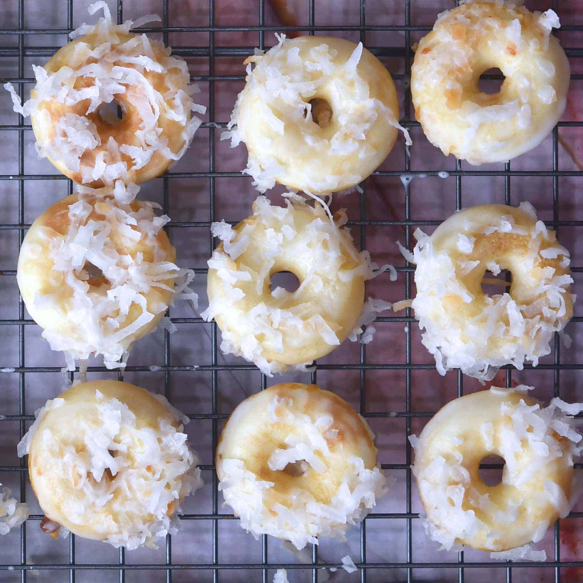 Coconut glazed donuts with unique flavors on a cooling rack.