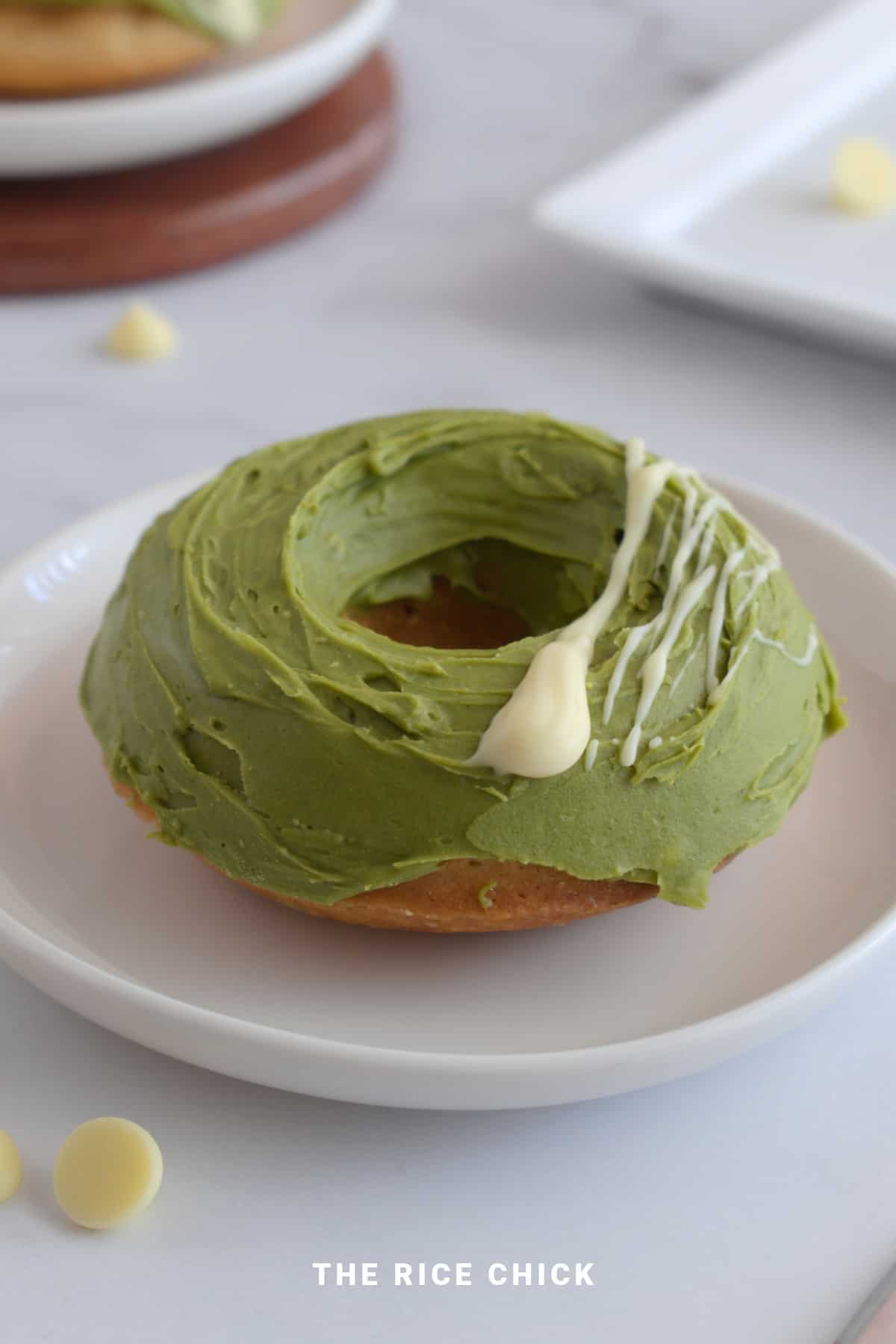 A unique donut with green frosting on a plate.