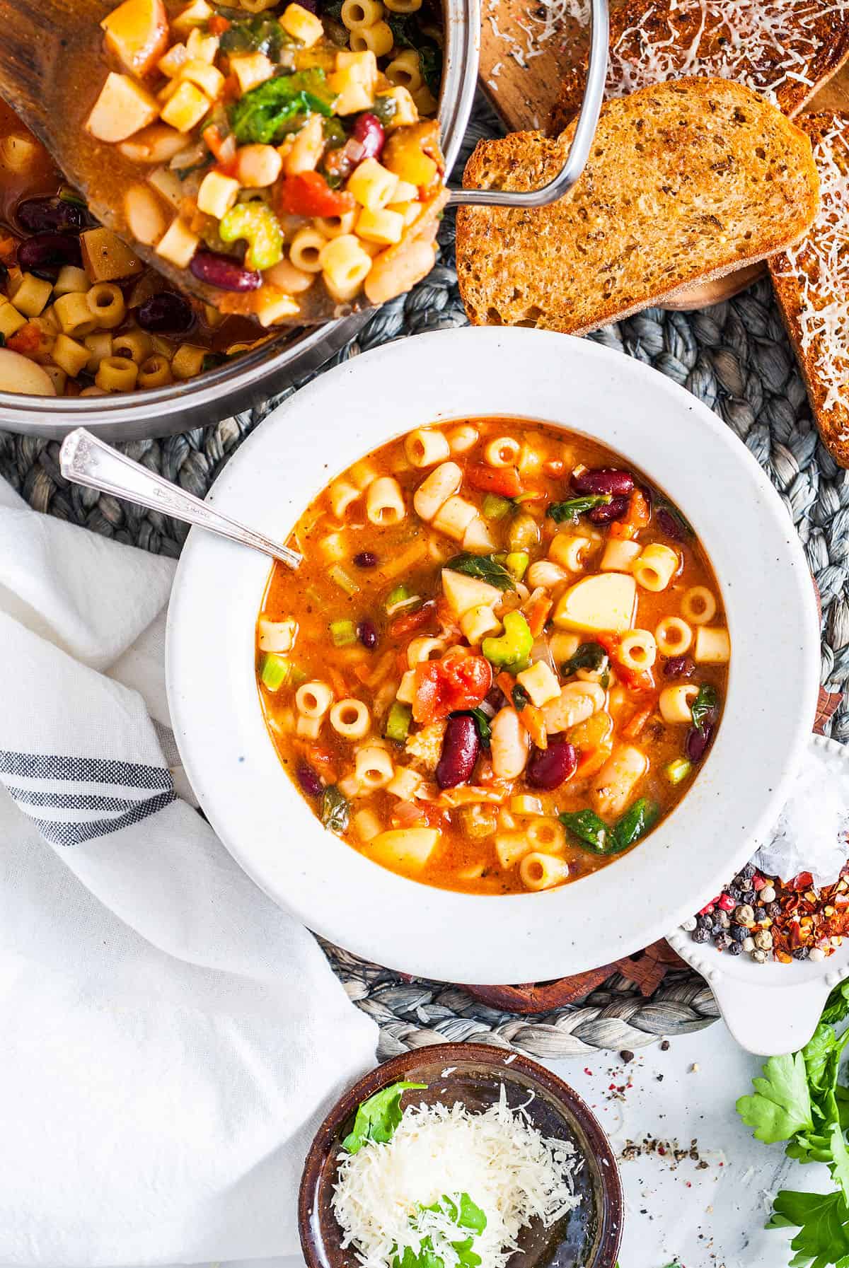 Overhead view of a bowl of homemade Italian minestrone soup. The pot of soup is beside the bowl. 
