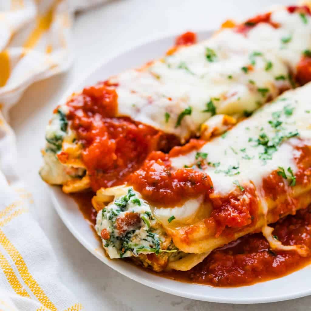 Serving two stuffed manicotti noodles on a white plate. 
