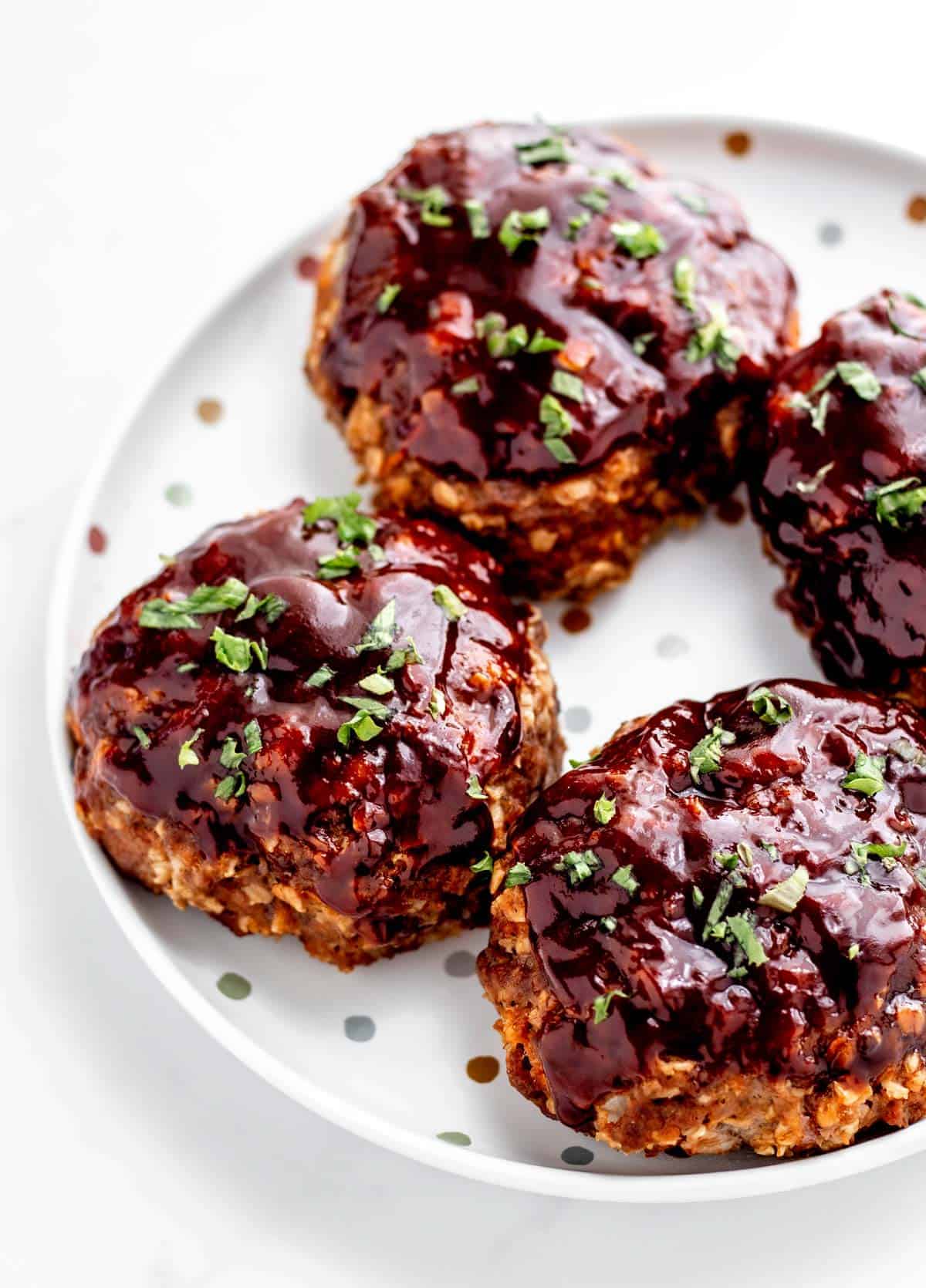 A plate with four mini meatloaves topped with glaze and parsley. 
