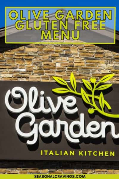 A sign for Olive Garden's Italian kitchen with the text "Olive Garden Gluten Free Menu" at the top. The background features a stone wall and some greenery.