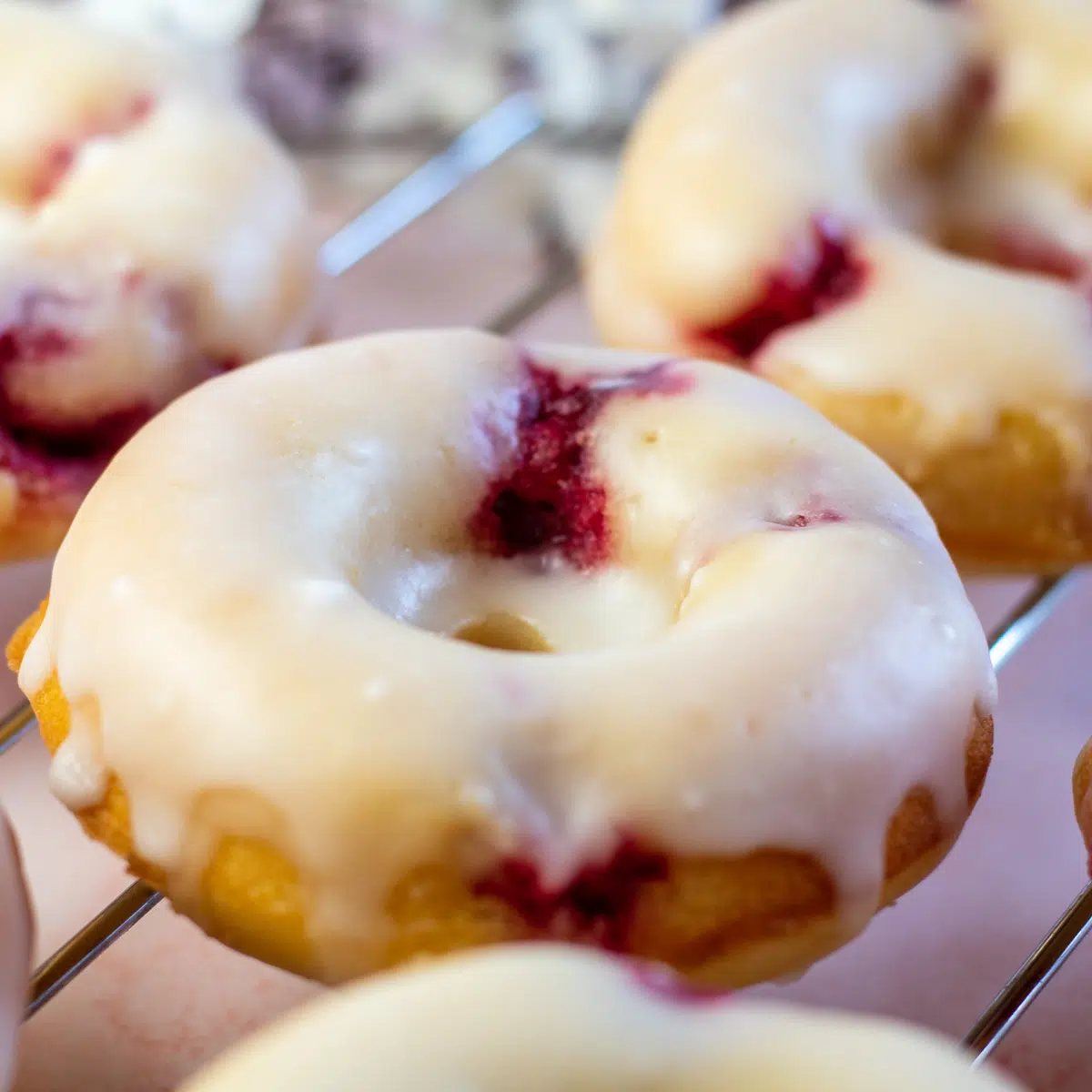 Raspberry glazed donuts, a unique donut flavor, on a cooling rack.