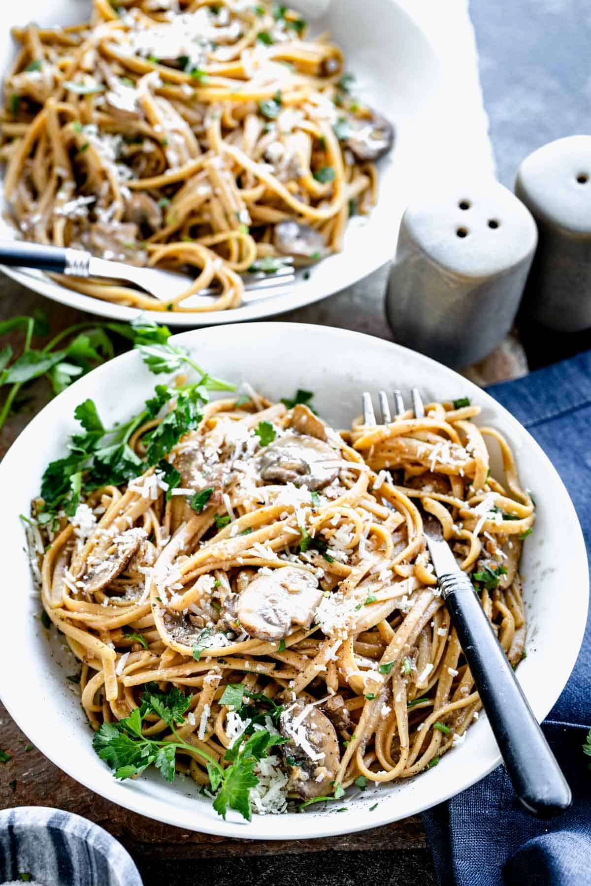 two bowls of Carbonara with mushrooms with cheese on top. 
