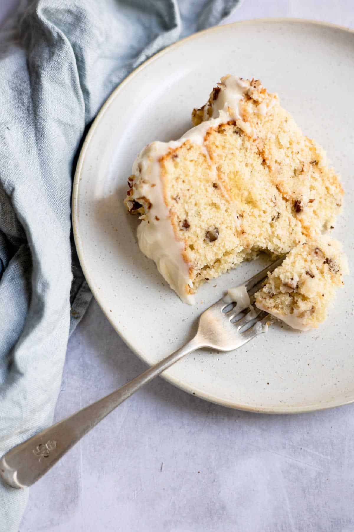 A slice of Italian cream cake on a plate with a fork taking a bite. 
