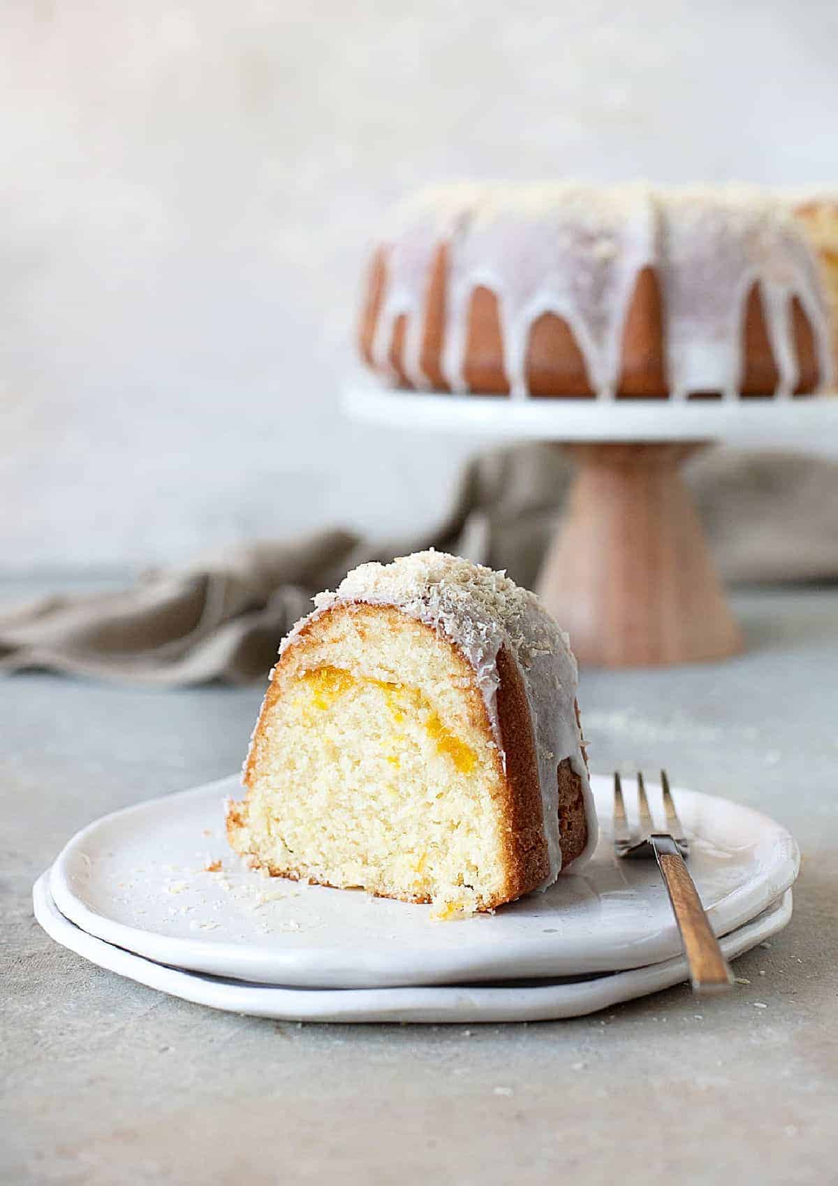 Glazed mango coconut bundt cake on a white plate. Cake stand in the grey background. Grey surface. 
