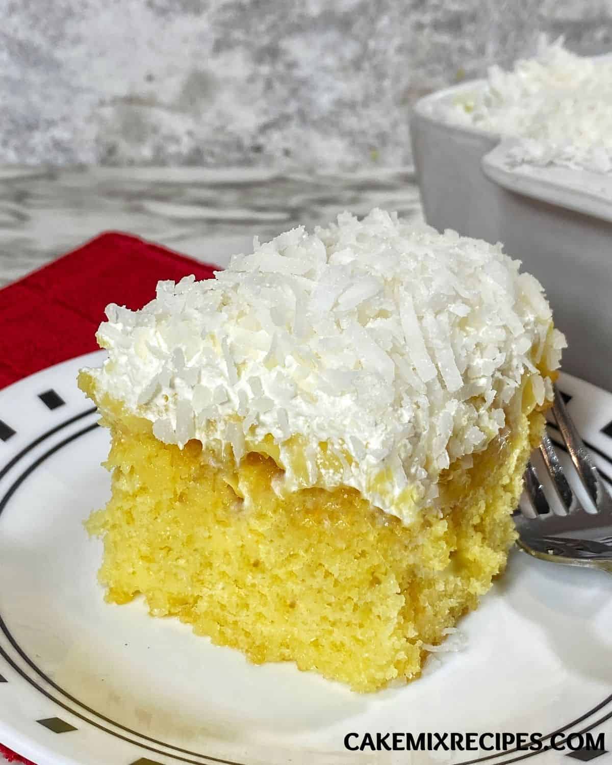 A slice of Pineapple Coconut Poke Cake on plate with a fork on the side. 
