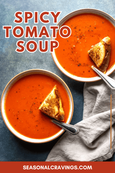 Two bowls of tomato soup labeled "Spicy Tomato Soup," each served with a grilled cheese sandwich triangle and a spoon, placed on a blue surface with a folded napkin. Text reads "seasonalcravinging.com.