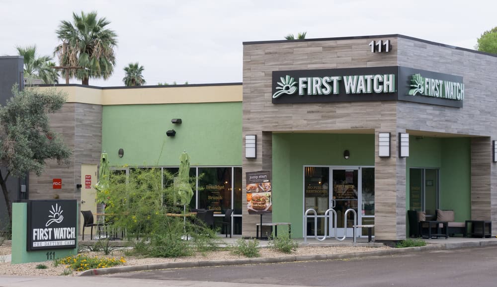 A First Watch restaurant exterior, featuring modern architecture with green and gray walls, and labeled with signage.